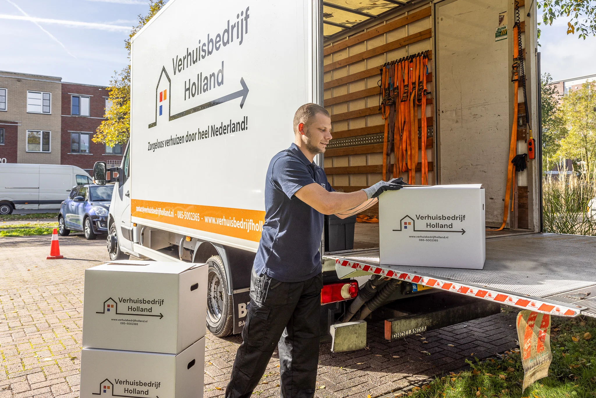 Verhuisbedrijf Woerden medewerker laadt verhuisdozen op laadklep van witte verhuiswagen